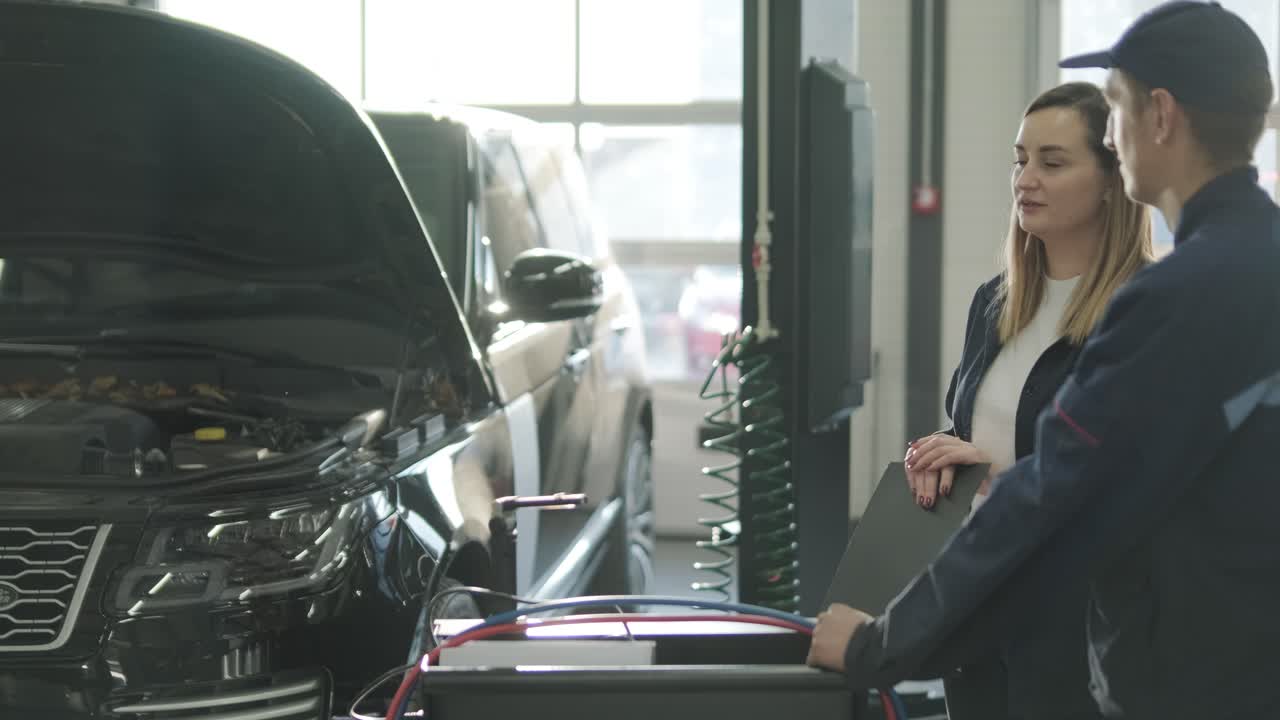 여성 매니저가 자동차 수리점에서 기계공과 함께 차량 수리를 논의하고 있습니다.