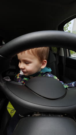 little caucasian toddler sitting on the driver's seat in the car. baby boy dusting the panels in the auto with a rag.