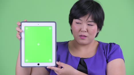 portrait of overweight asian woman with short hairstyle showing chroma key from digital tablet against green background