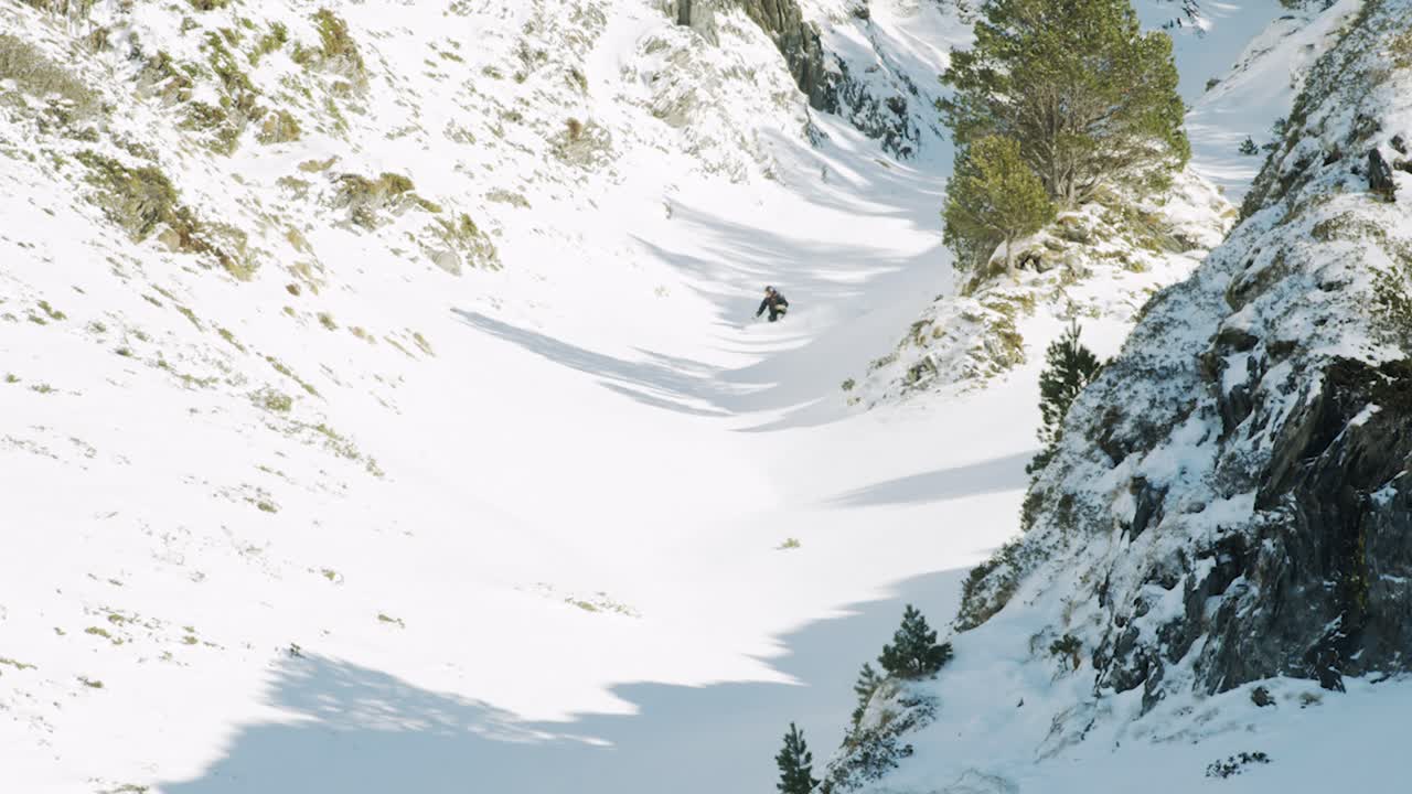 vista en cámara lenta de un hombre esquiando libremente y girando en un barranco cubierto de nieve en polvo profunda en un hermoso día soleado