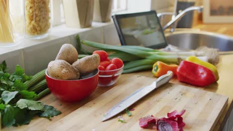 close up of wooden countertop with vegetables on chopping board and tablet in kitchen