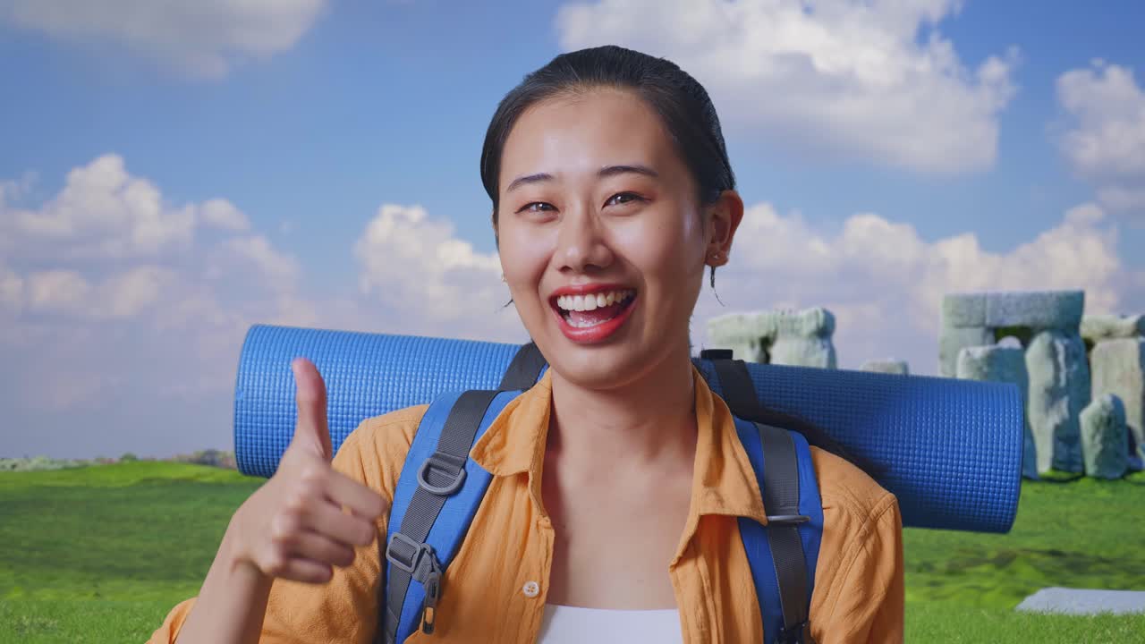 Close Up Of Asian Female Hiker With Mountaineering Backpack Smiling And Showing Thumbs Up Gesture To Camera While Traveling In Stonehenge