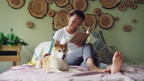 woman reading a book with a dog on a bed