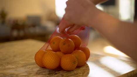 still shot of a man grabbing an orange from a red net bag