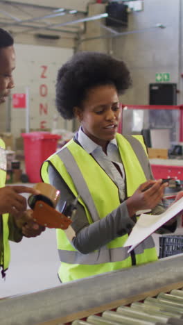 african american male and female workers with clipboard next to conveyor belt in warehouse