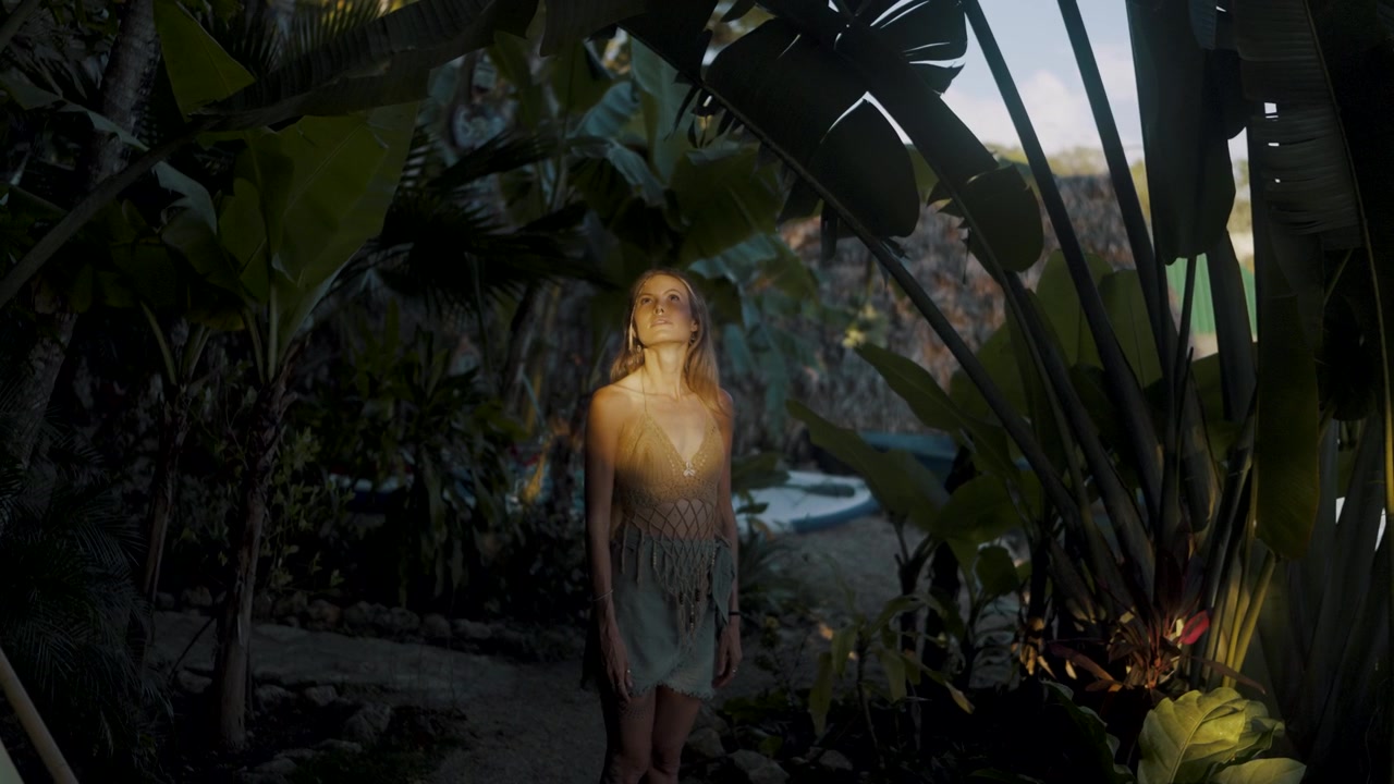 Žena v splývavých šatech stojí uprostřed náladové džungle osvětlené soumrakem ve Flores, Petén, Guatemala.