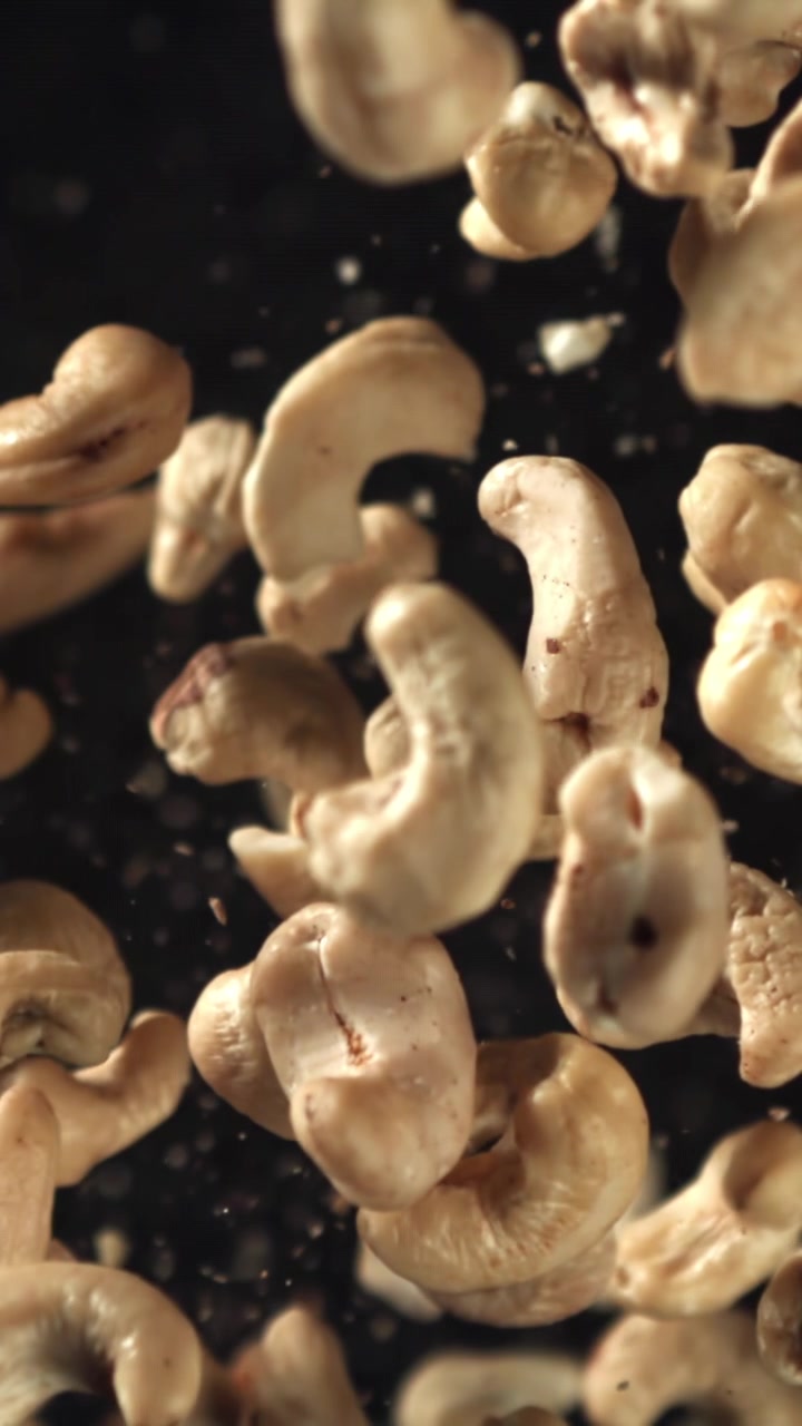 Nærbilde av cashewnøtter som faller i sakte film på svart bakgrunn