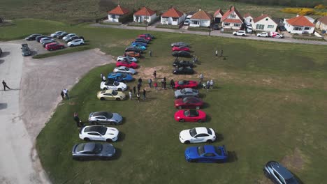 Aerial-drone-forward-moving-shot-over-vertical-rows-of-supercars-parked-outside-the-Flamborough-Head-Lighthouse-in-Flamborough,-UK-at-daytime