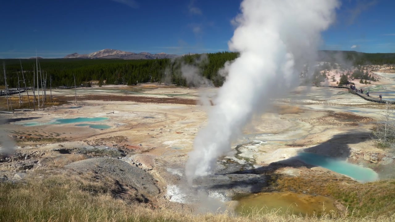 Mata air panas Norris Geyser Basin dengan uap bergejolak di Taman Nasional Yellowstone Wyoming. Pemandangan alam panas bumi yang indah di Artist Paintpot, Porcelain Basin, Back Basin. Musim gugur dengan langit biru cerah dan jalur pejalan kaki.
