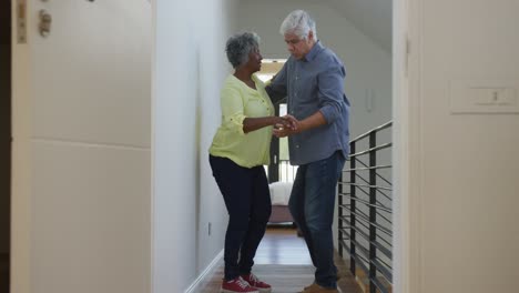 Happy-senior-diverse-couple-dancing-in-corridor-at-retirement-home