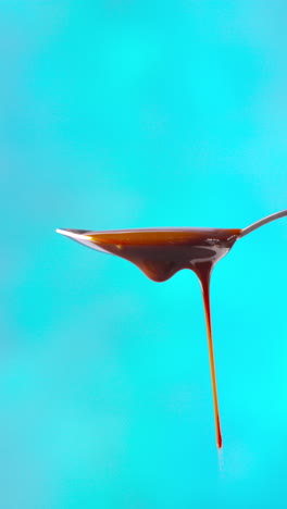 vertical video of melted chocolate dripping from overflowing spoon against blue coloured background with copy space