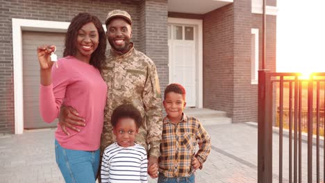 portrait of african american family of army officer with little kids moving in new house and showing keys