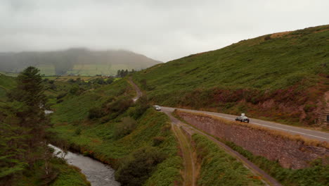 Vorwärtsfliegen-über-Der-Straße-Auf-Dem-Land-An-Bewölkten-Und-Dunstigen-Tagen.-Autos-Fahren-Entlang-Des-Fließenden-Baches-Im-Tal.-Irland