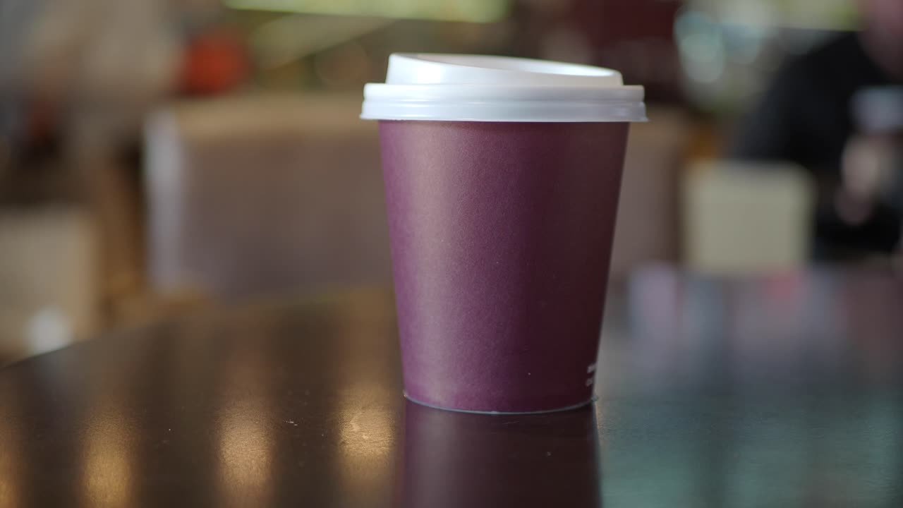 primer plano de una taza de café de papel púrpura con una tapa blanca en una mesa