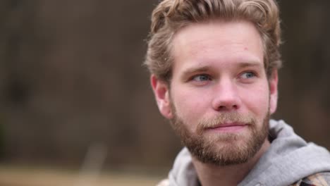 this bearded young man is captured by a unique camera movement as he watches something in the distance with a slight grin on his face