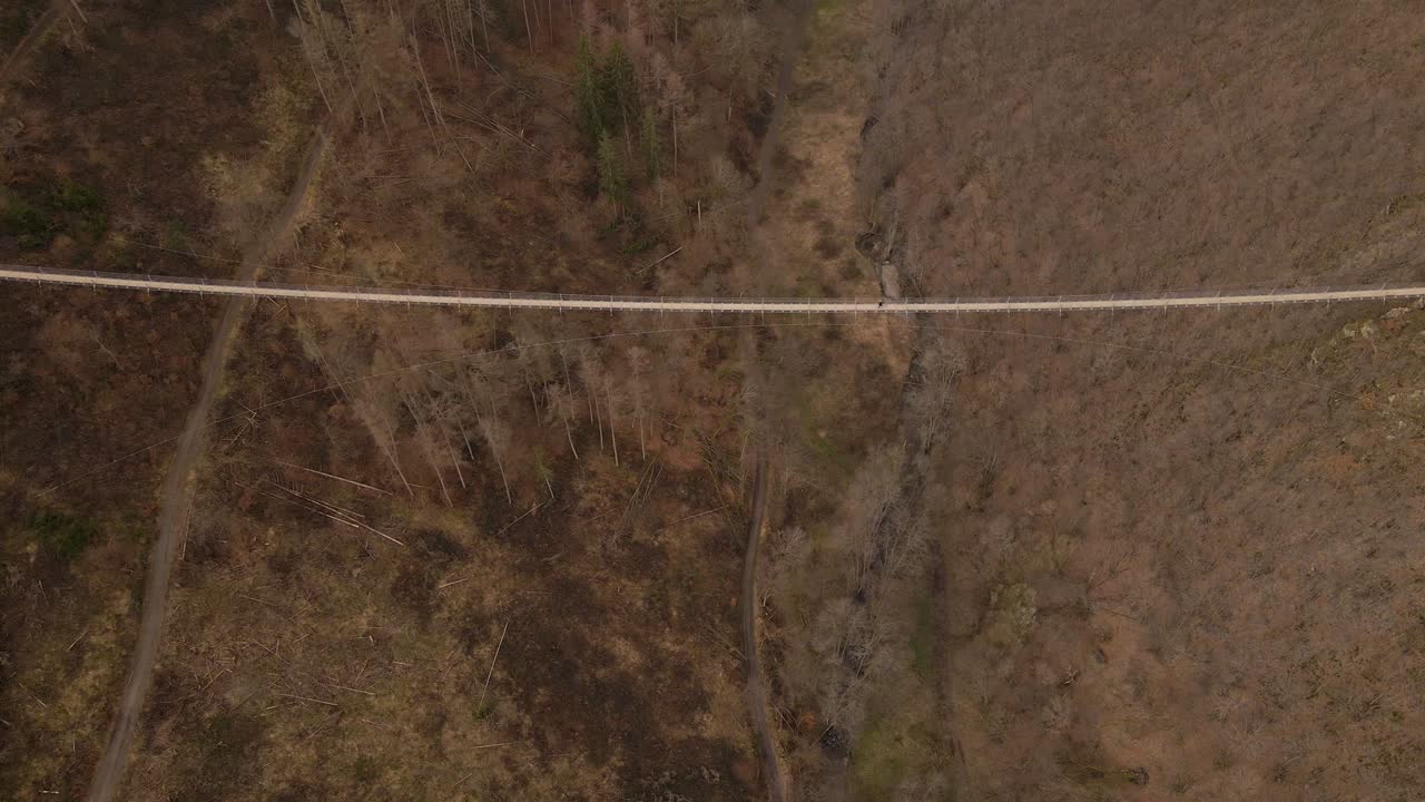 Aerial high angle reveal shot of a tourist crossing Germany's longest suspension bridge on a dry winter day