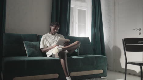 champ sitting on teal sofa, reading tablet with full attention in cozy, modern living room. soft light flows through window, creating a peaceful atmosphere with a minimalist design