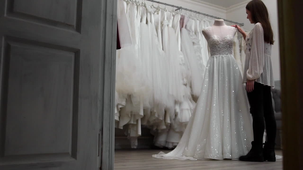 bella ragazza vestito da sposa in cabina rispetto ad altri abiti. preparazione per il matrimonio. l'acquisto di un abito da sposa. la sarta ispeziona il vestito da sposa finito su misura.