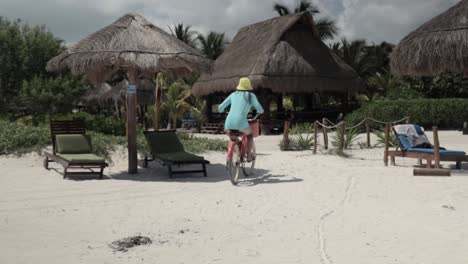 mujer caucásica montando una bicicleta en la playa, usando una camisa azul de protección solar