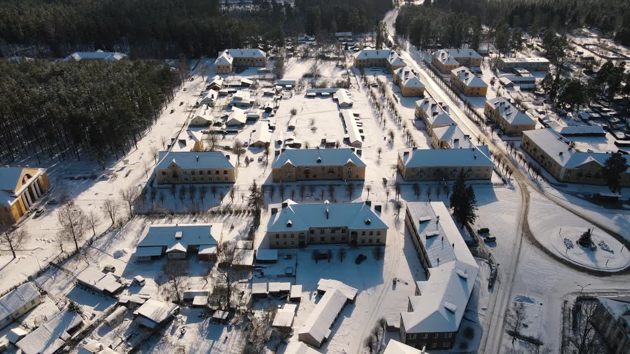 Aerial view of the snow-covered small town of Seda with yellow buildings, streets and roofs covered in white. A peaceful winter landscape in the sunlight.