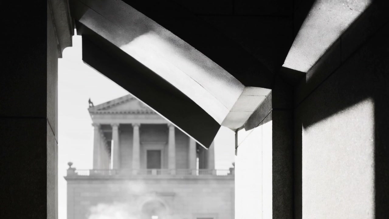 Opening covered passage revealing neoclassical facade, diagonal beam casting shadows, haze rising