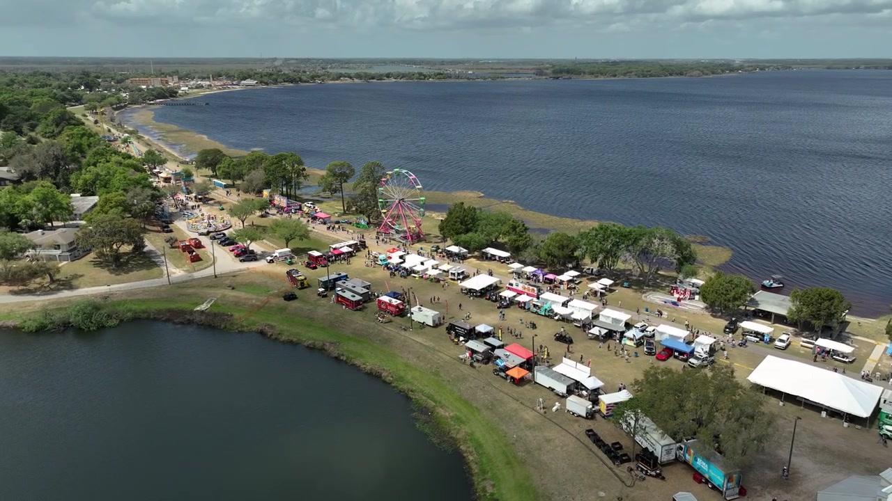 Vista aerea con drone del festival Pig on the Pond a Clermont, Florida, che mostra un vivace luna park in riva al lago, una ruota panoramica, stand gastronomici e folle che si godono l'evento.
