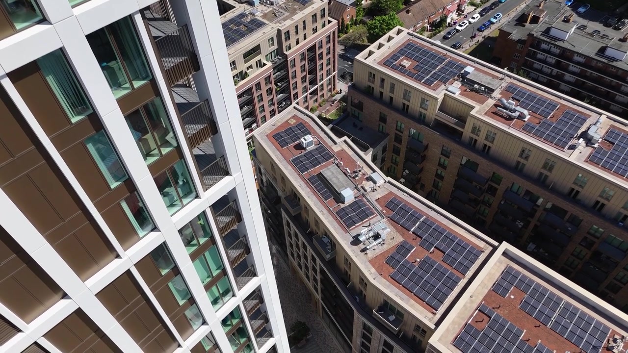 Painéis solares nos telhados de novos edifícios de apartamentos vistos de cima, ao lado da fachada de vidro de uma torre residencial.