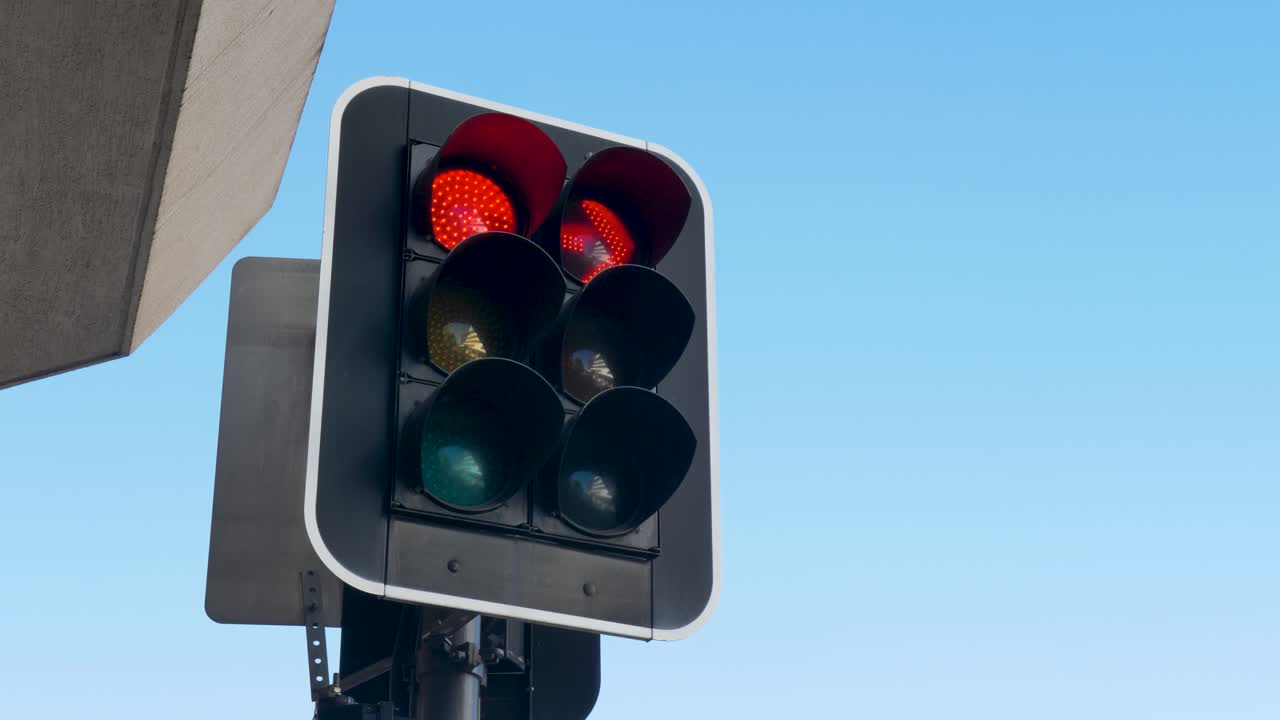 Slow motion landscape of a green traffic stoplight signal turning to orange and then a red arrow with the sky in the background in Gosford city street CBD Australia travel transport and infrastructure