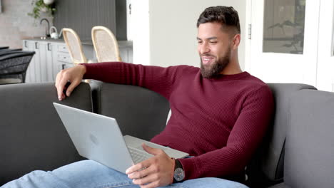smiling man using laptop and raising fist while sitting on couch at home