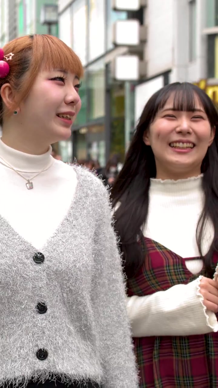 หญิงสาวสองคนเดินผ่านย่านฮาราจูกุ ชี้ชวนและพูดคุยกันอย่างตื่นเต้นระหว่างการเดินทางช้อปปิ้งในเวลากลางวัน