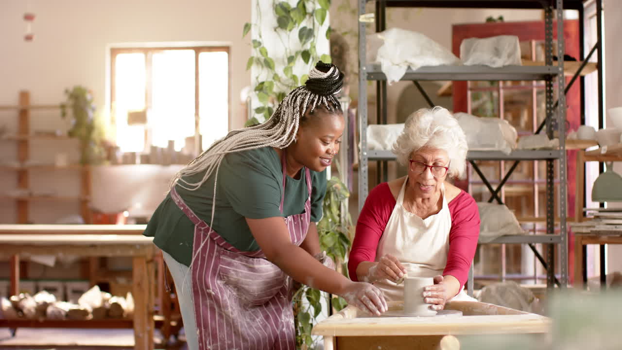 Focused diverse female potters using potter's wheel in pottery studio, slow motion