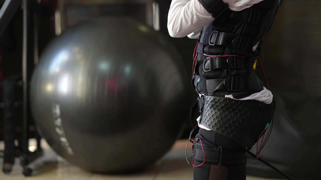 요가 공 을 사용 하여 운동 을 하기 위해 ems 의복 을 착용 하는 여자