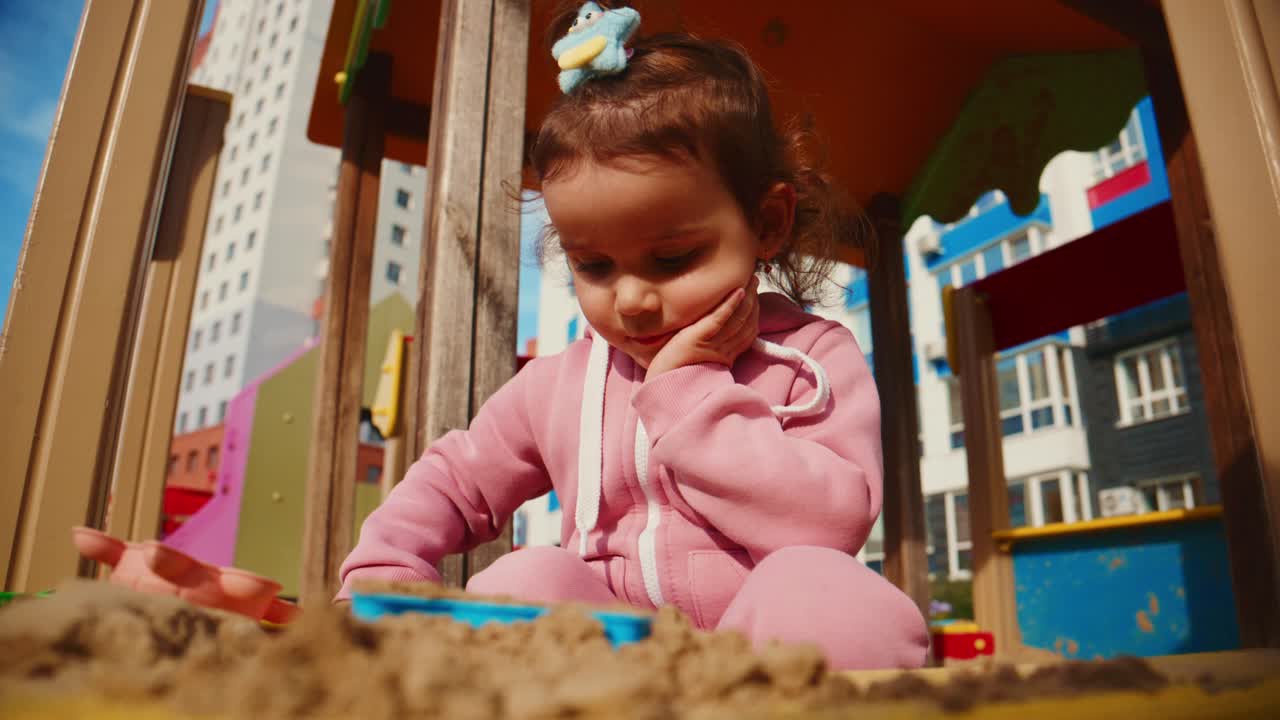 A Curious Child Enjoys Playtime in a Sandbox, Engaged with Colorful Toys Beneath a Clear Blue Sky, Showcasing Exploration and Imagination