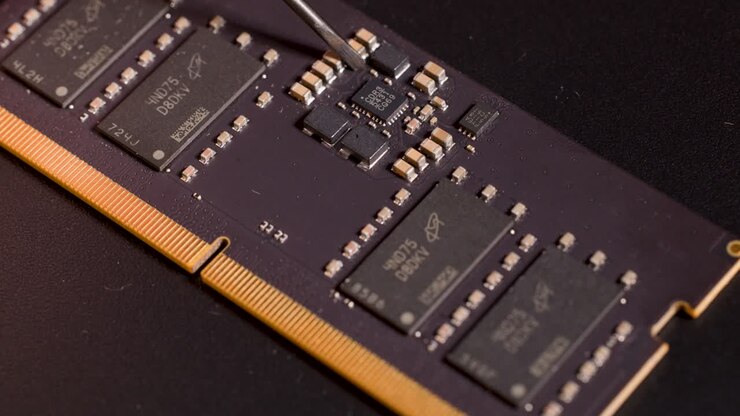 Strumento in metallo che punta con precisione a un microchip su una scheda di circuito di memoria sotto illuminazione controllata da studio