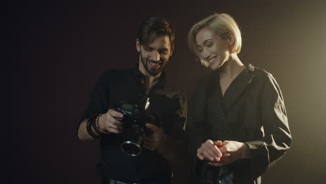 caucasian male photographer and female model watching photos on the camera screen in dark studio