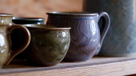 a collection of handcrafted ceramic pottery and mugs on a wooden shelf
