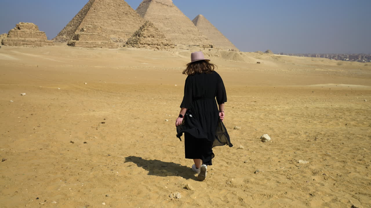 suelo arenoso con una chica vestida de negro caminando hacia las grandes pirámides de giza en el cairo, egipto