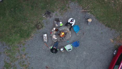 Top-down-view-of-two-people-sitting-around-campfire,-one-person-looking-at-his-phone