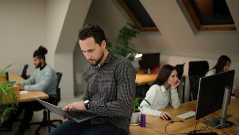 Focused-caucasian-young-man-sitting-on-the-table-with-laptop,-trying-to-solve-the-problem