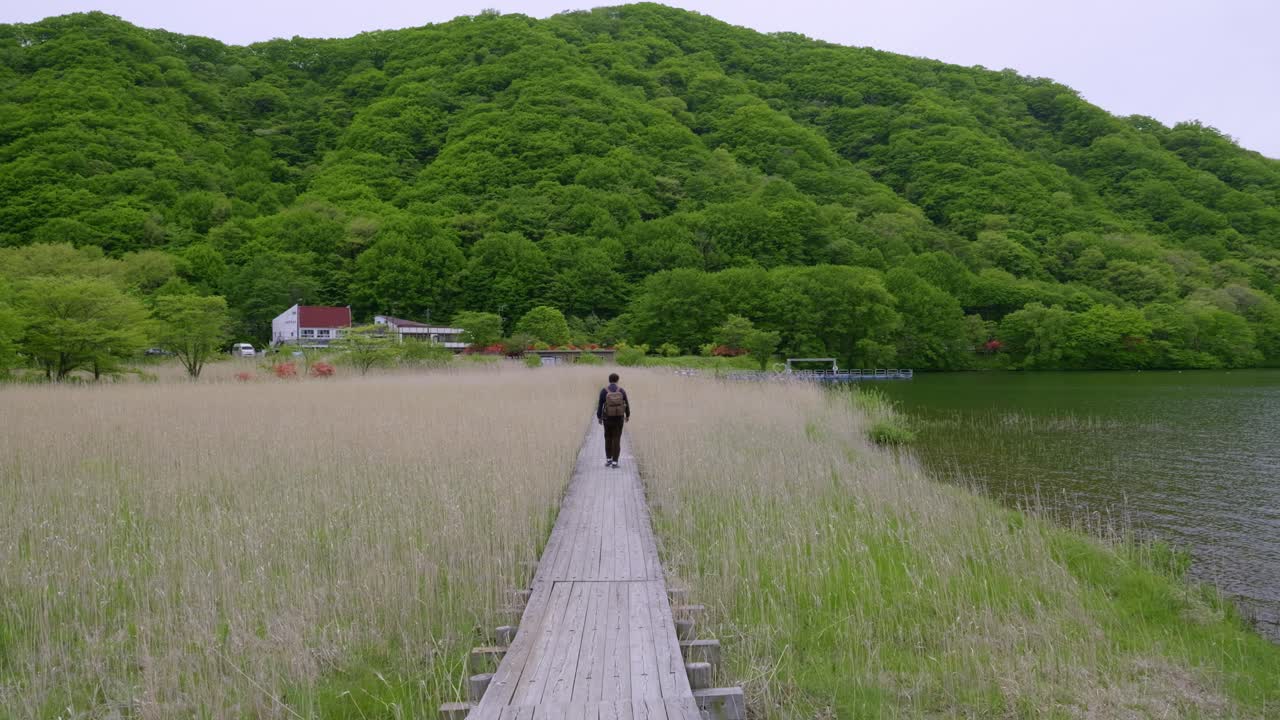 Male hiker walking through beautiful landscape with tall grass and lake