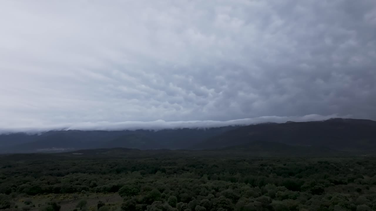Dark Mammatus clouds loom over the lush Tiétar Valley and surrounding mountains in Ávila, Spain. Aerial view shows dramatic spring contrast between vibrant landscape and stormy sky in May