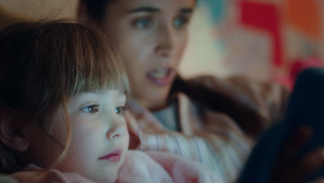hermosa niña usando una tableta con su madre enseñando a su hija jugando juegos en la tecnología de pantalla táctil relajándose divirtiéndose antes de acostarse