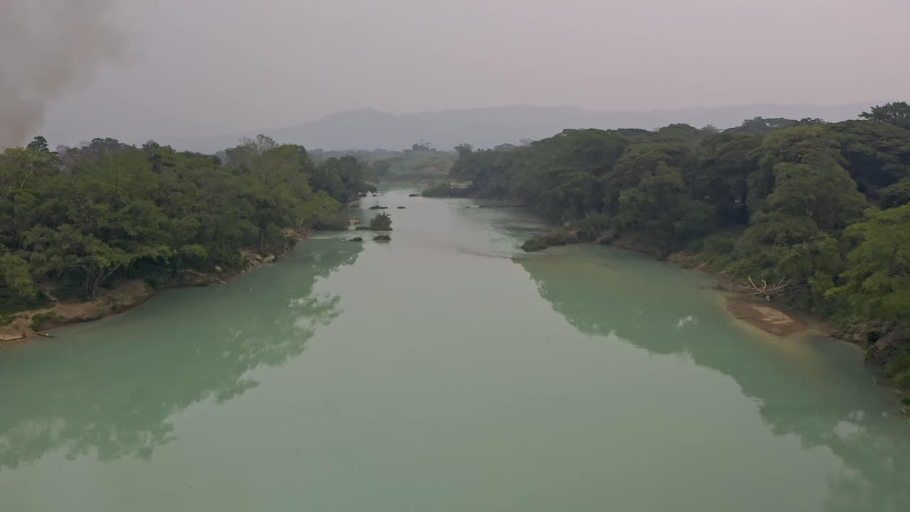 Aerial Drone shot in the Agua Clara in Chiapas, México. The light-colored river water is spanned by a long, rustic footbridge, on which a lone man is seen crossing It