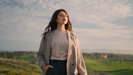 Stylish-woman-standing-grass-in-front-beautiful-cloudy-sky.-Serious-girl-posing.