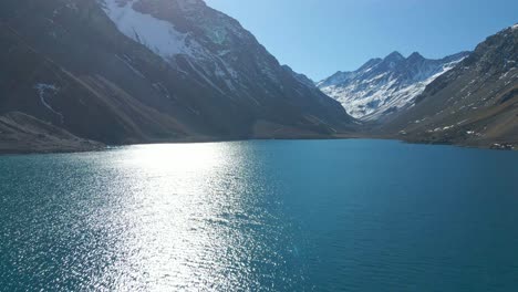 Aerial-elevation-view-of-Laguna-del-Inca-in-the-Chilean-Andes,-with-the-snowcapped-mountains-in-the-background-on-a-sunny-day