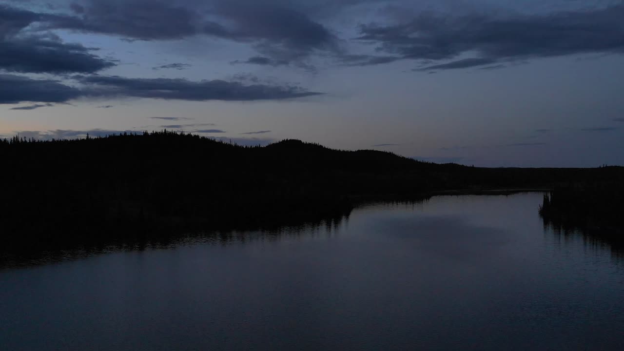 4K-video dronen lentäessä tummien vesien yllä ja lähestyessä järvenrantaa iltahämärässä
