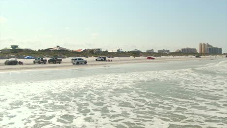 Una-Vista-Aérea-Baja-Hacia-Adelante-De-Los-Automóviles-Que-Conducen-Sobre-La-Arena-En-La-Playa-De-New-Smyrna,-Florida