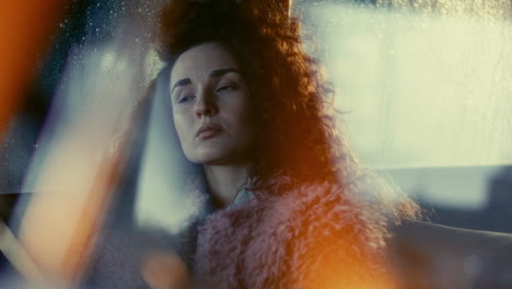 Melancholic Girl in Fluffy Coat Leaning against Rain-Streaked Window in Car