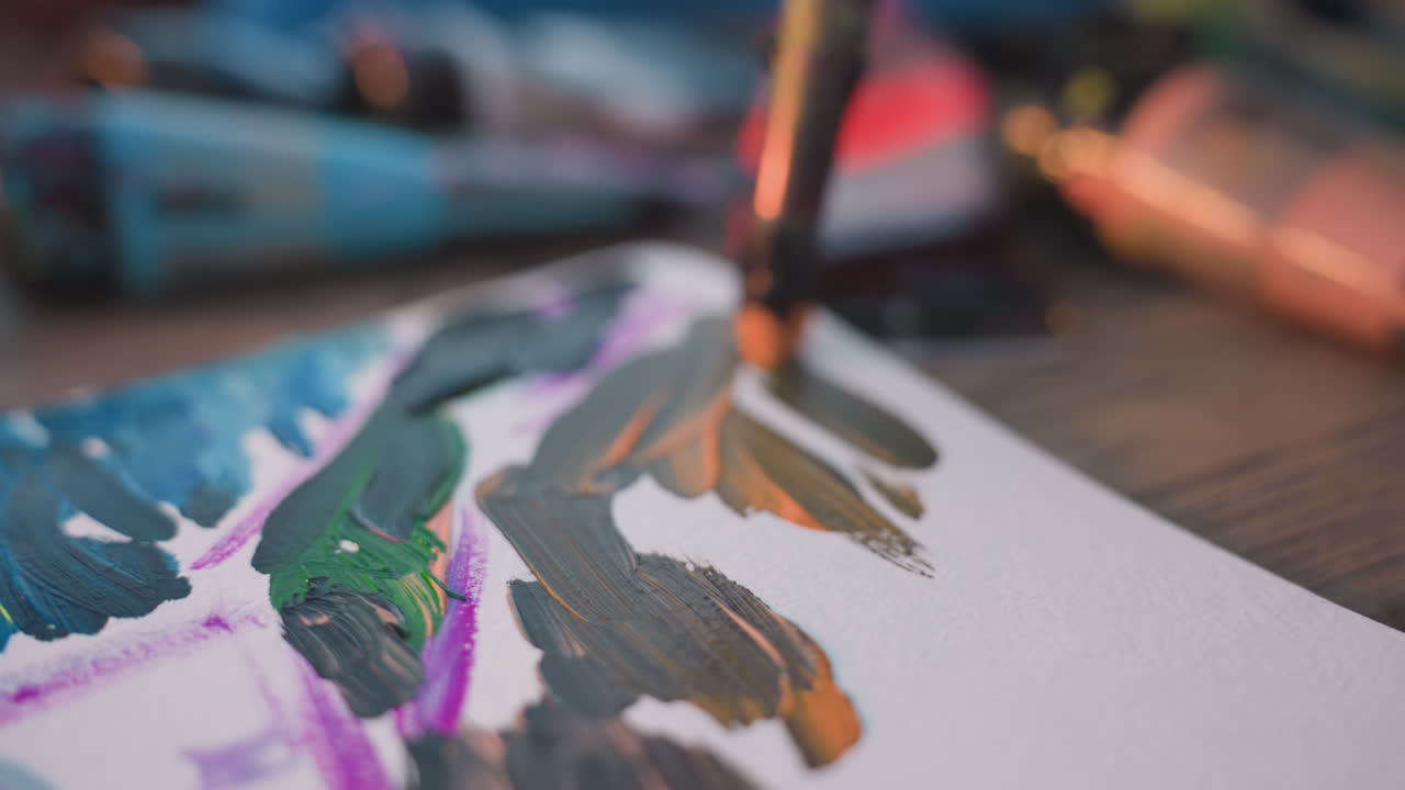 close up of illustrator hand painting vibrant tower sketch on white sheet, paintbrush strokes blending acrylic pigments, supplies scattered on wooden table under warm sunlight