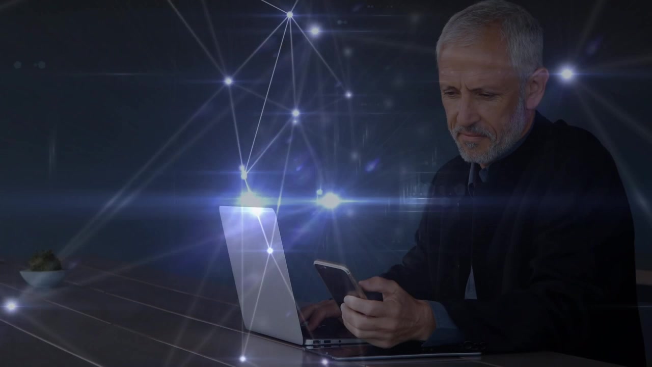 Leuchtendes Netzwerk von Verbindungen über einem kaukasischen älteren Geschäftsmann mit Laptop, der ein Smartphone benutzt